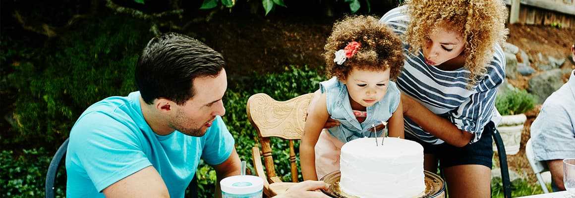 Parents with child who is blowing out candles on a birthday cake