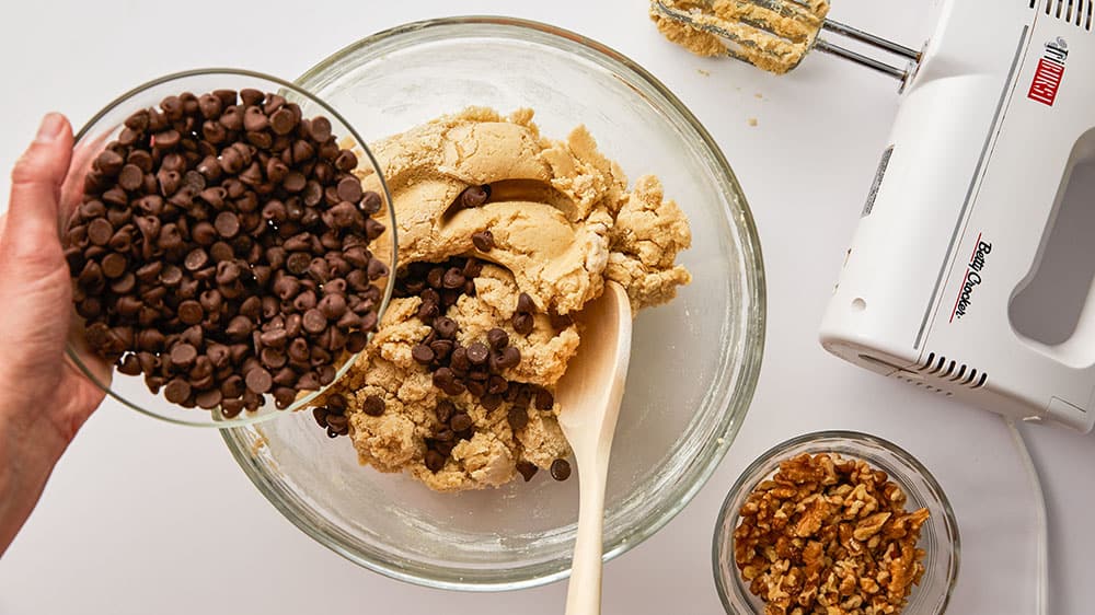 pouring chocolate chips into cookie dough