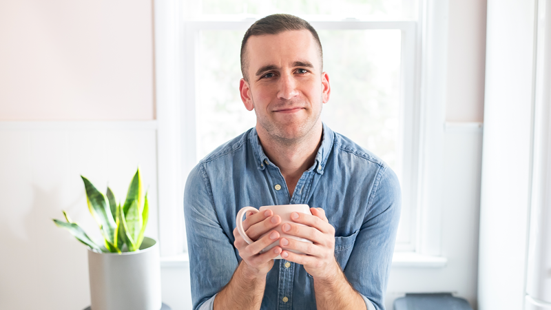 Josh Lehenbauer looking at the camera leaning on a counter holding a mug with both hands