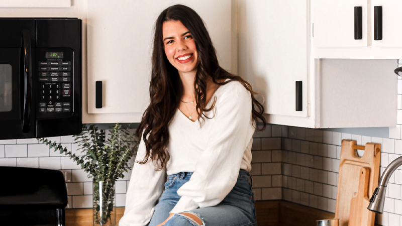 Marley Braunlich smiling at the camera, sitting on the countertop in the kitchen